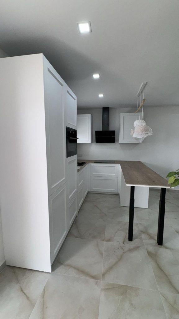 Vista completa de cocina blanca clásica en U con columnas altas y península de madera