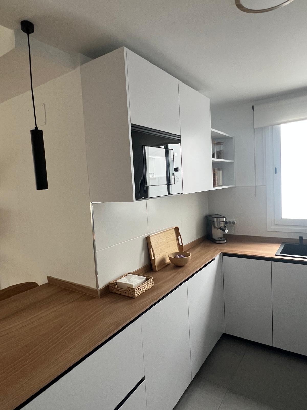 Cocina blanca en L con encimera roble y campana negra