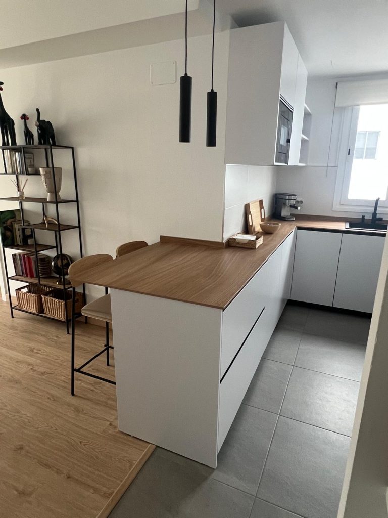 Cocina blanca minimalista con península de madera roble abierta al comedor con estantería lateral