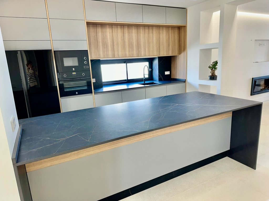 Cocina de alta gama con frentes gris mate, madera nogal e isla Dekton negro con vetas doradas