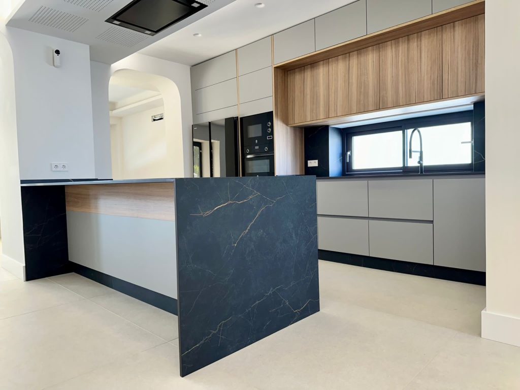 Detalle isla Dekton negro veteado y frentes gris mate con complementos madera nogal